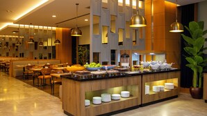 Um hall de hotel moderno com área de buffet central, disposição de assentos e uma grande planta em vaso.