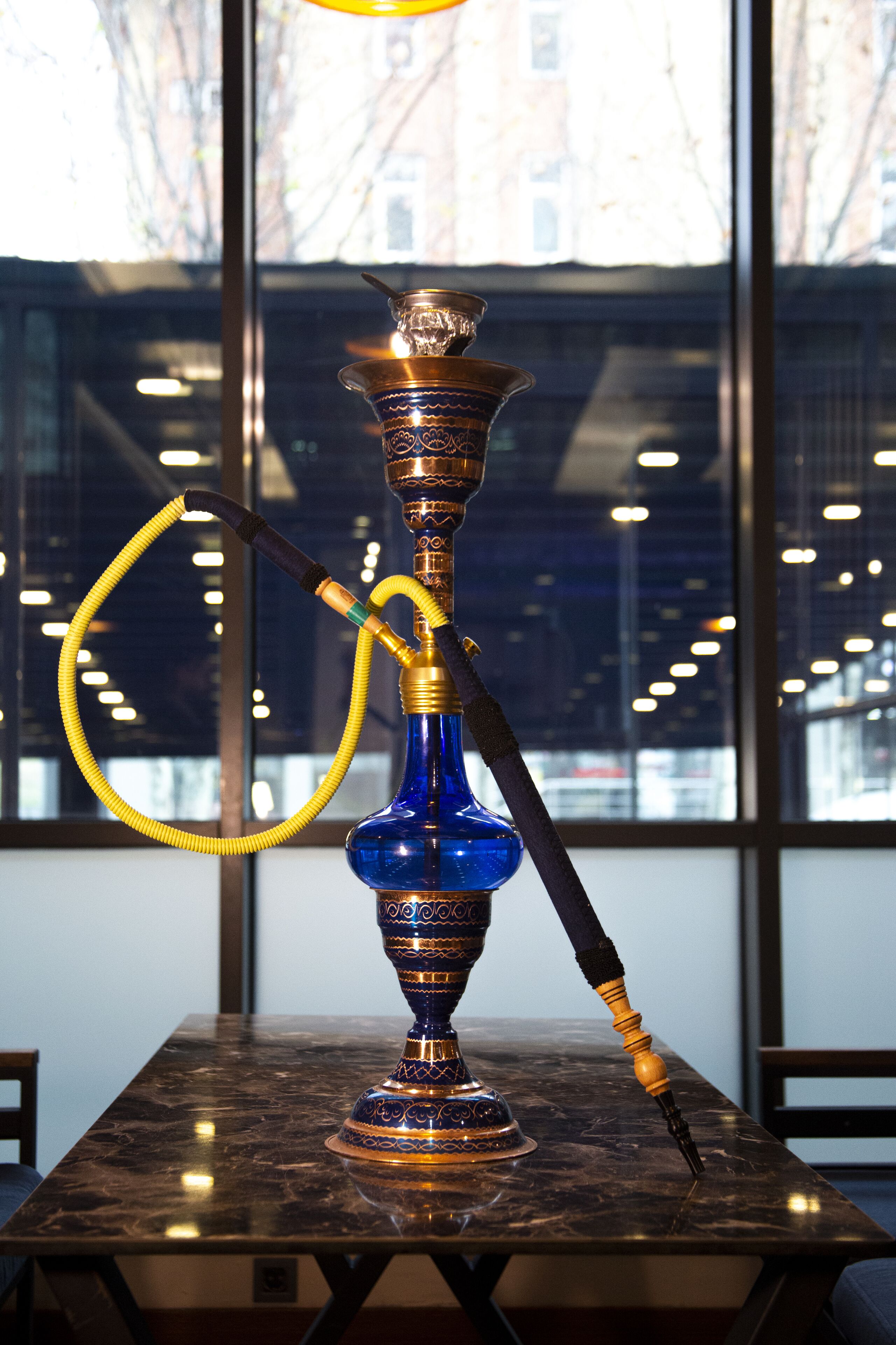 A hookah on a marble table with a view of buildings through a window.