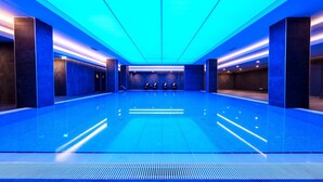 Uma ampla piscina interior com design moderno, com área de estar central e teto iluminado em azul.
