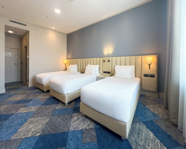A hotel room with two beds, a large window, and a carpeted floor.