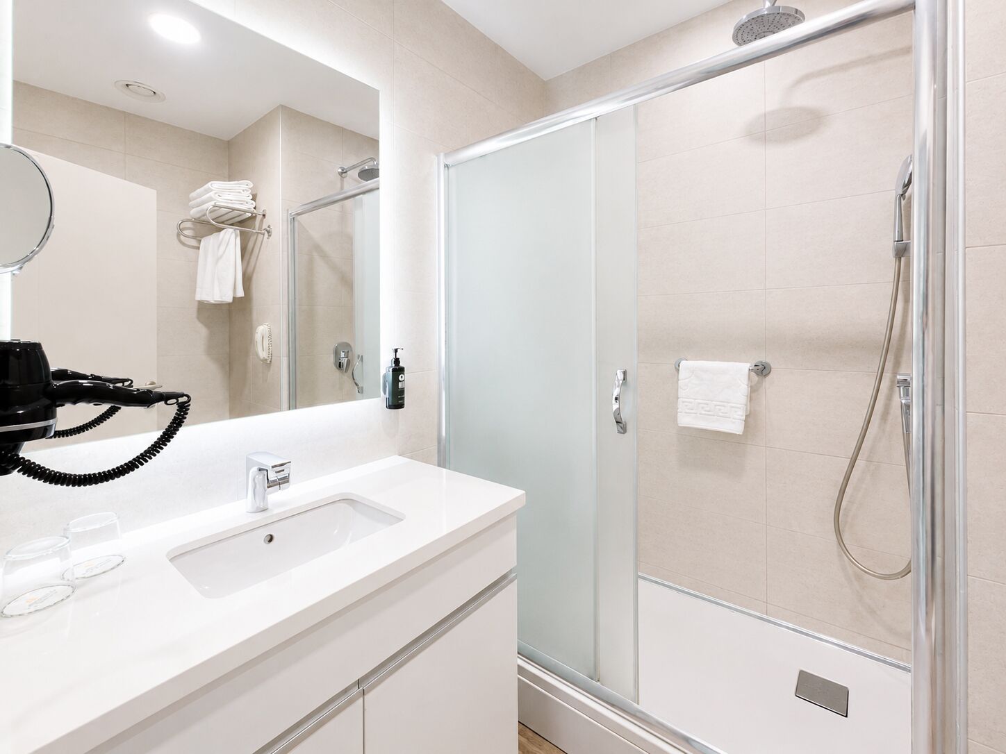 A modern bathroom with a glass-enclosed shower, a white sink, and a hairdryer on the counter.