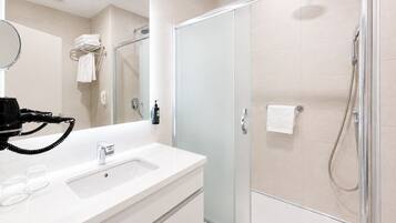 A modern bathroom with a glass-enclosed shower, a white sink, and a hairdryer on the counter.