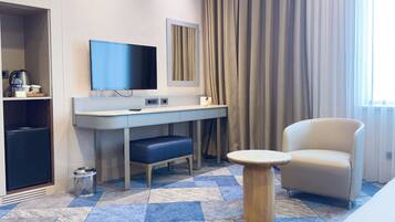A hotel room with a desk, chair, television, and a large window with curtains.