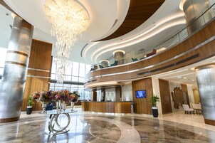 A modern hotel lobby with a reception desk, a chandelier, and a large plant.
