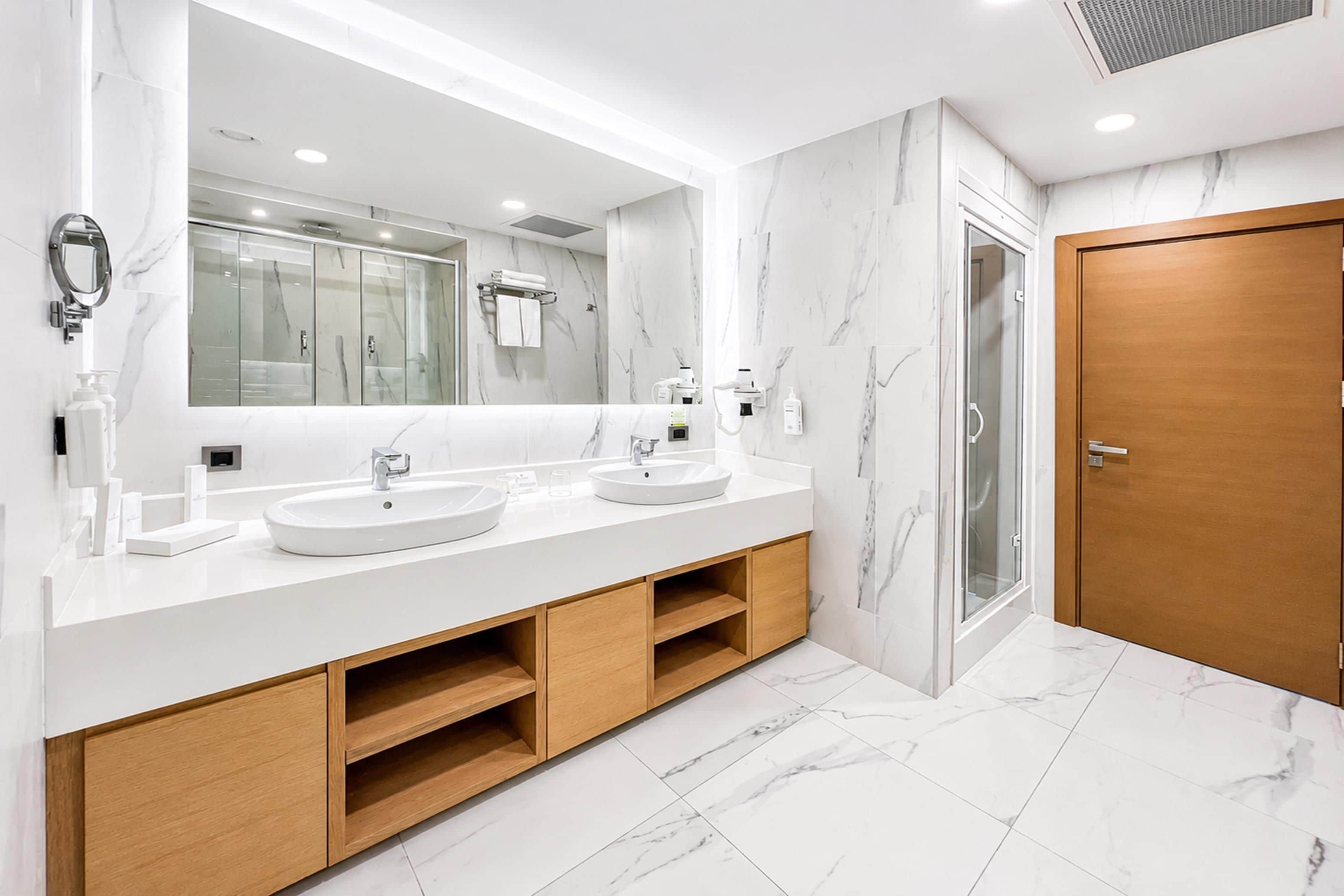 A modern bathroom with two sinks, a large mirror, and a shower.