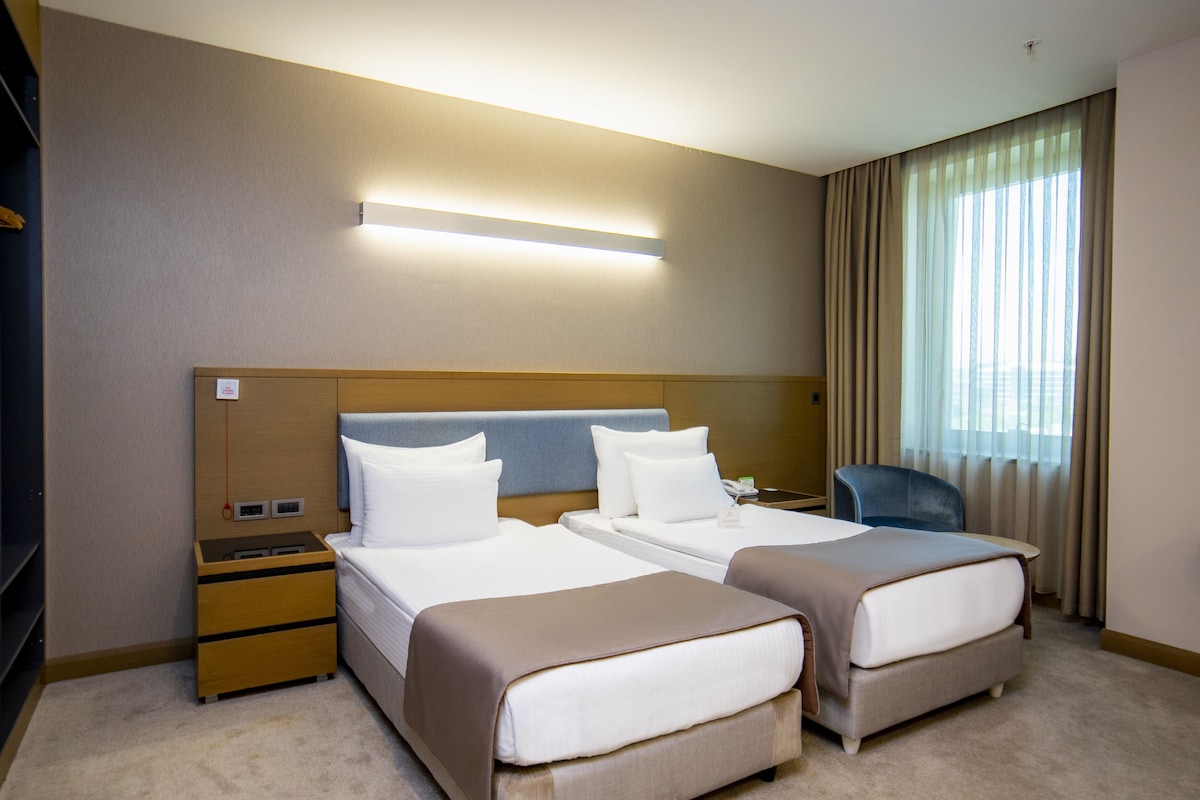 A hotel room with two beds, a nightstand, a desk, and a chair.