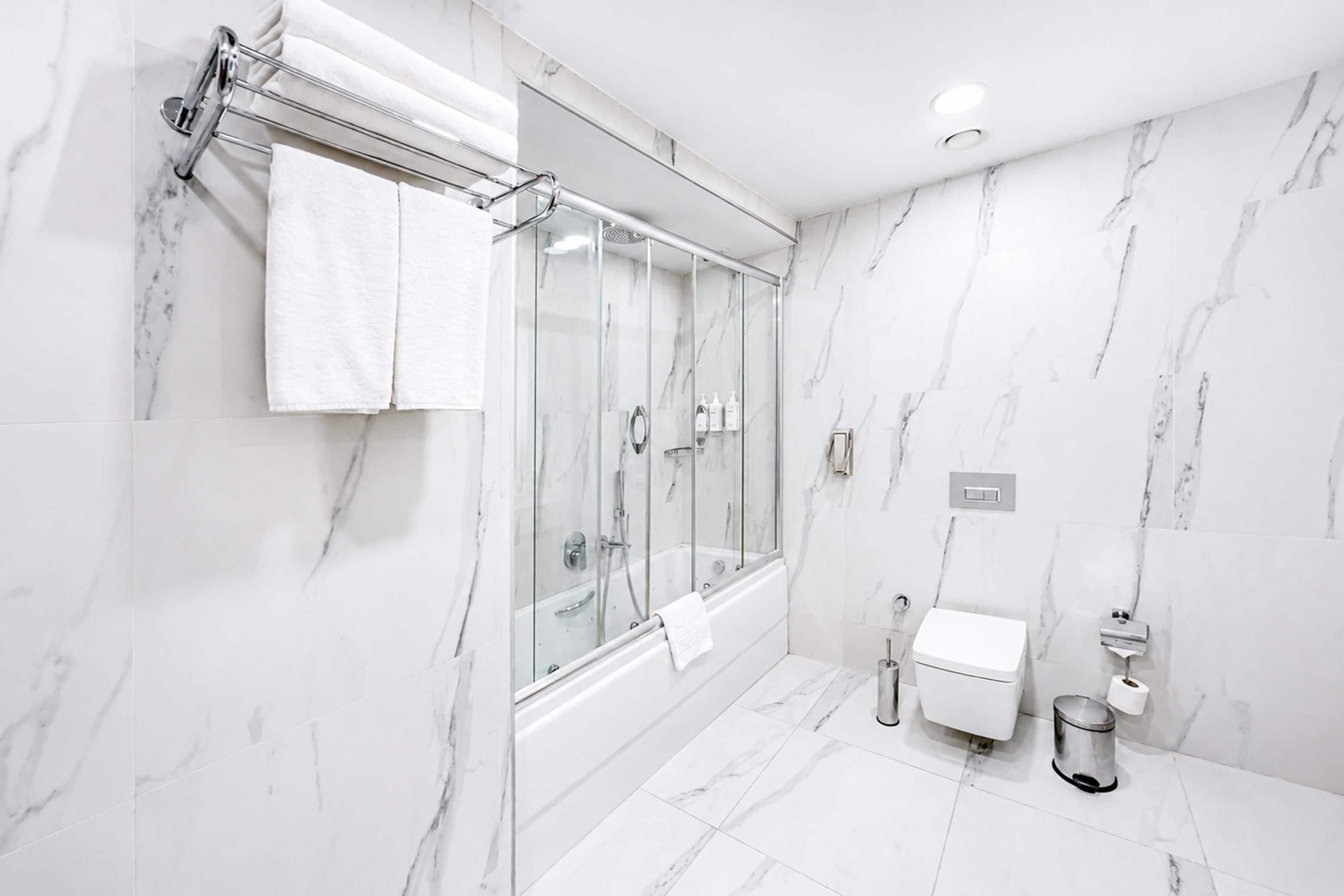 Casa de banho moderna com chuveiro envidraçado, paredes de mármore branco e sanita branca.