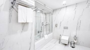 Casa de banho moderna com chuveiro envidraçado, paredes de mármore branco e sanita branca.