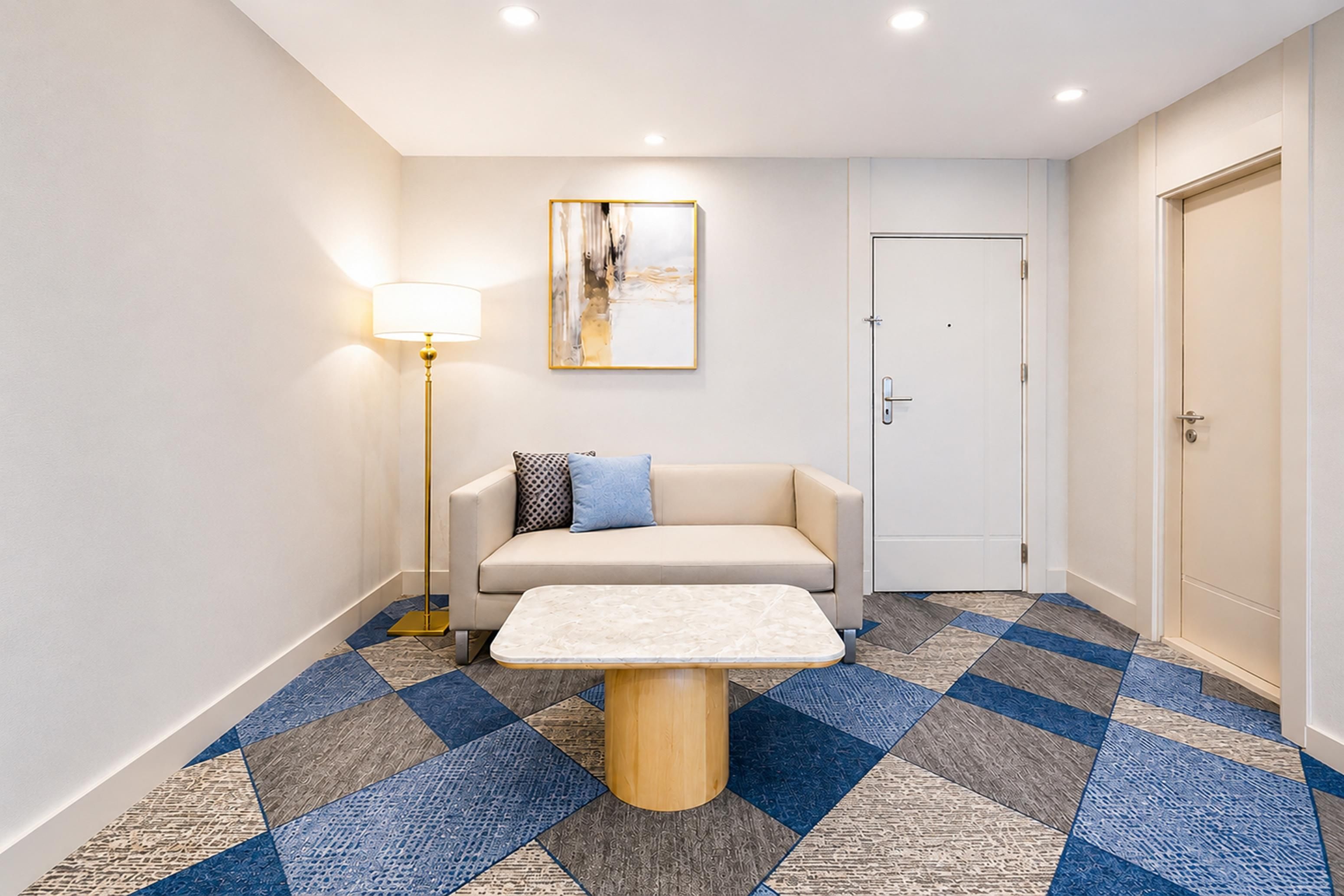 A hotel lobby with a sofa, a coffee table, a floor lamp, a painting, and a door.