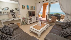 Un salon comprenant un canapé, un téléviseur, une table basse et donnant sur la plage.