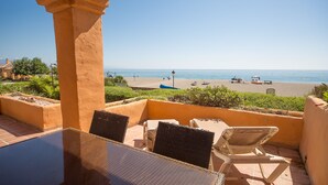 Une terrasse avec vue sur la plage, comprenant une table et des chaises, et un ciel dégagé.