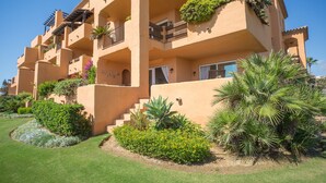 Un immeuble à plusieurs étages doté de balcons, d’un jardin bien entretenu et surplombant un ciel dégagé.