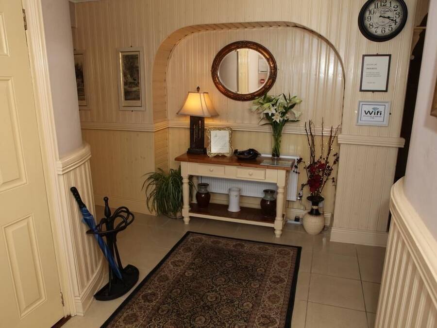 Un couloir avec une console en bois, un miroir, une horloge et un vase rempli de fleurs.