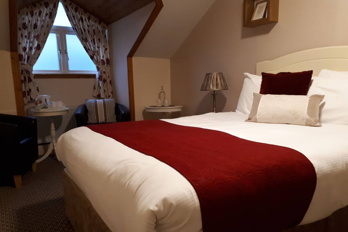 A hotel room with a large bed, a desk, a chair, a lamp, and a window with curtains.