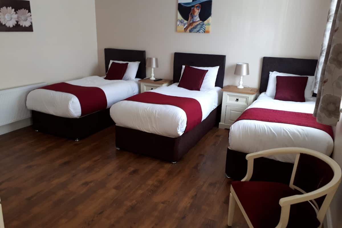 A hotel room with two beds, each with white bedding and red accents, a wooden floor, and a chair.