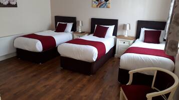 A hotel room with two beds, each with white bedding and red accents, a wooden floor, and a chair.