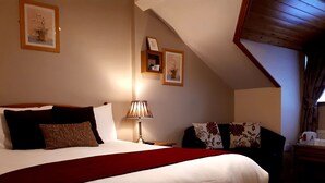 A bedroom with a large bed, a bedside table with a lamp, a chair with floral cushions, and framed pictures on the walls. - Jim McGee's (Wexford)