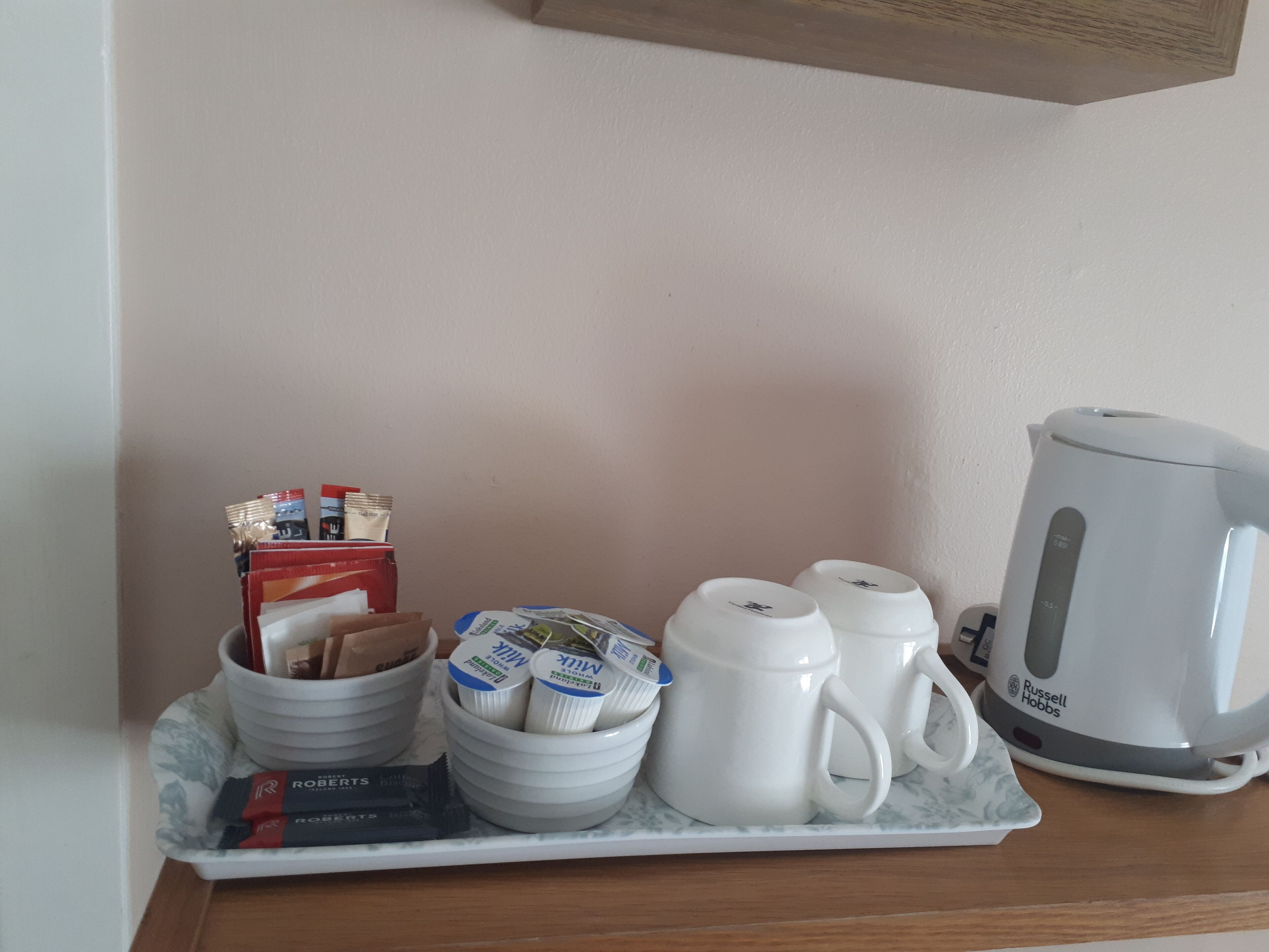 A breakfast tray with milk cartons, coffee mugs, and a tea kettle on a marble table.