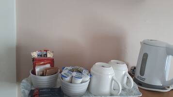 A breakfast tray with milk cartons, coffee mugs, and a tea kettle on a marble table.