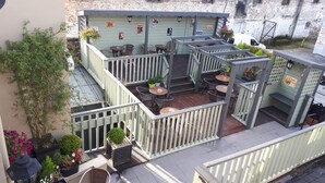 An outdoor patio area with multiple seating arrangements, including tables and chairs, surrounded by potted plants and a wooden deck. - Jim McGee's (Wexford)