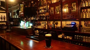 A bar with a Guinness beer tap and a variety of bottles and glasses on shelves. - Jim McGee's (Wexford)