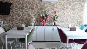 Un comedor con una mesa blanca, sillas verdes y rojas, un papel tapiz floral y un televisor en la pared.