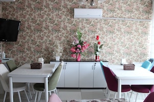 Un comedor con una mesa blanca, sillas verdes y rojas, un papel tapiz floral y un televisor en la pared.