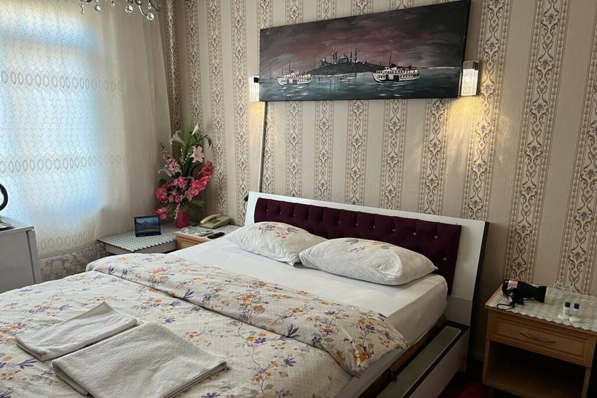 A neatly made bed with floral bedding, a nightstand with a lamp, and a painting of a ship on the wall.