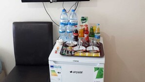 Una habitación con una televisión negra montada en la pared, un refrigerador pequeño lleno de bebidas y una silla negra.