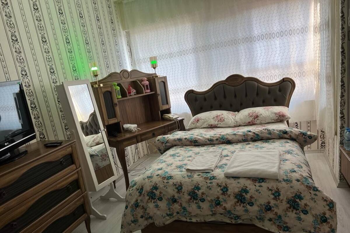 A bedroom with a wooden bed, a bedside table with a lamp, a mirror, and a dresser.
