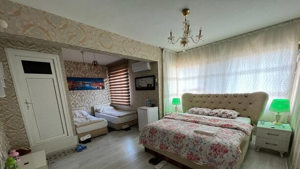 Un dormitorio con una cama, dos mesitas de noche, un armario, una ventana con cortinas y una araña.