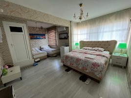 Un dormitorio con una cama, dos mesitas de noche, un armario, una ventana con cortinas y una araña.