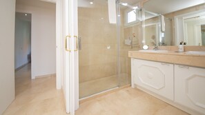 Un baño moderno con cabina de ducha de vidrio, tocador blanco con encimera de mármol y un espejo grande.