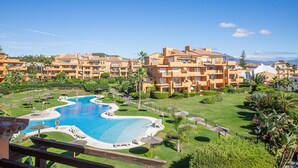 A resort with a central swimming pool, multiple-story buildings, and a well-maintained lawn with umbrellas. - Los Granados de la Duquesa 1522 (Manilva)