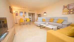 A modern living room with a sofa, coffee table, and yellow chairs. There is a dining area with a table and chairs. - Los Granados de la Duquesa 1711 (Manilva)