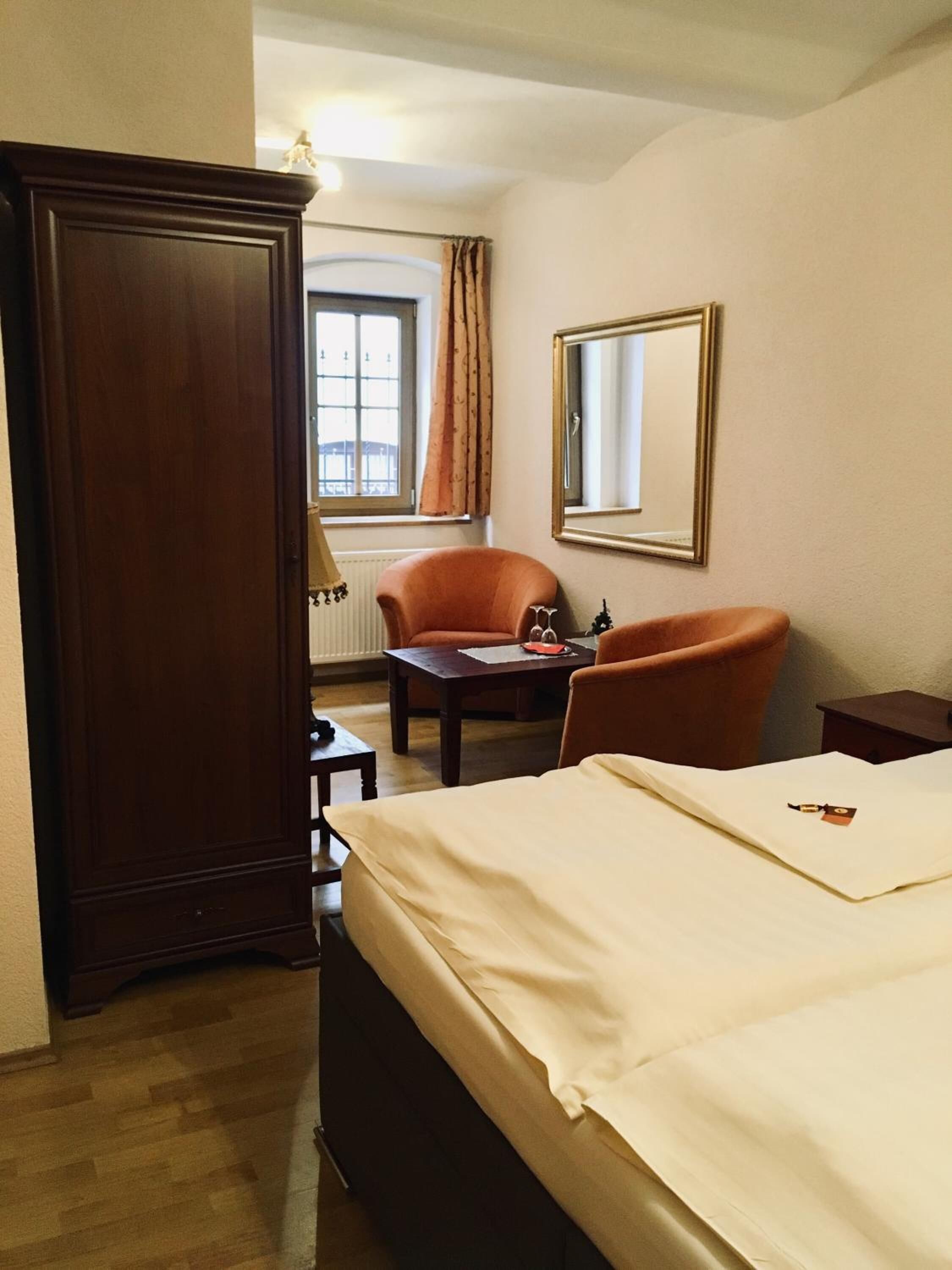 Una habitación de hotel con una cama, dos sillones, una mesita, un espejo y un armario.