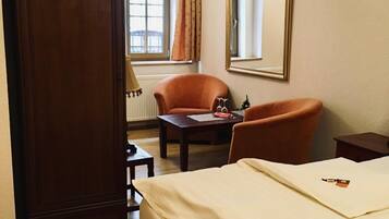 Una habitación de hotel con una cama, dos sillones, una mesita, un espejo y un armario.
