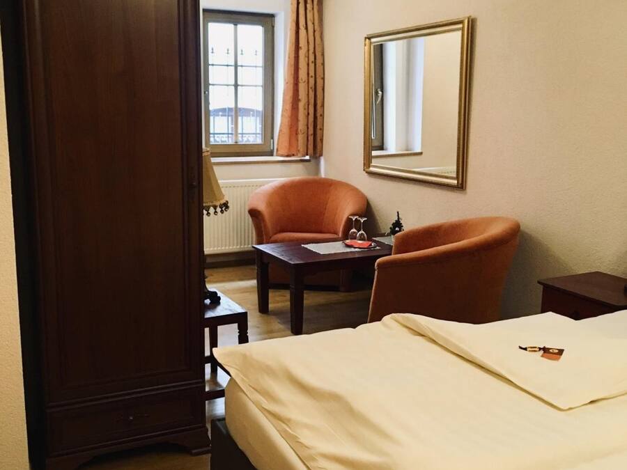 Una habitación de hotel con una cama, dos sillones, una mesita, un espejo y un armario.