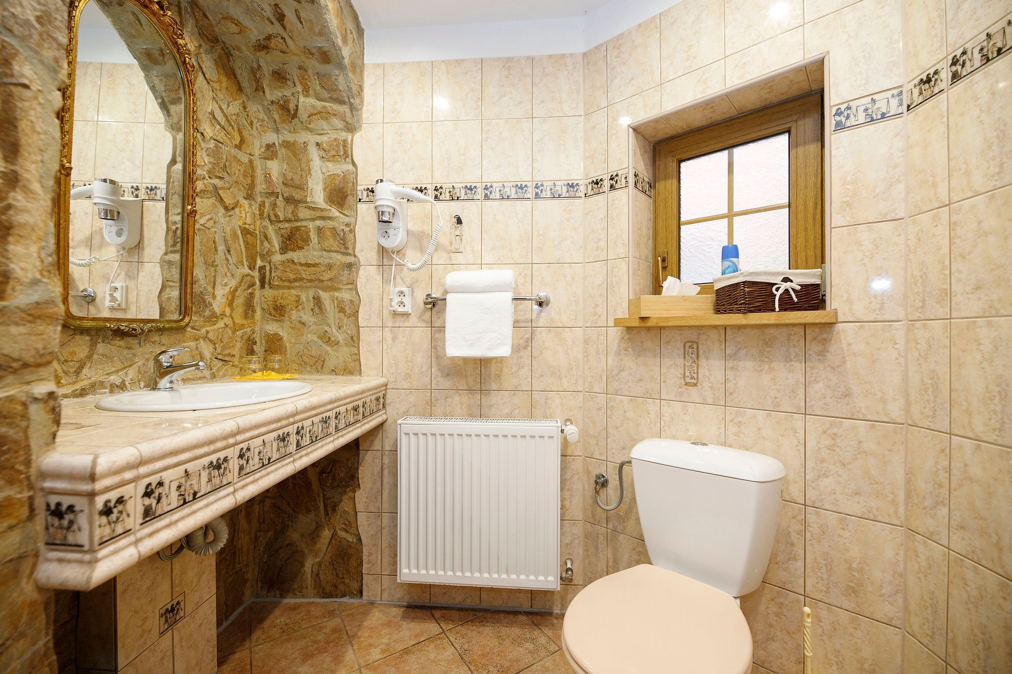A bathroom with a stone wall, a sink, a toilet, a window, and a towel rack.