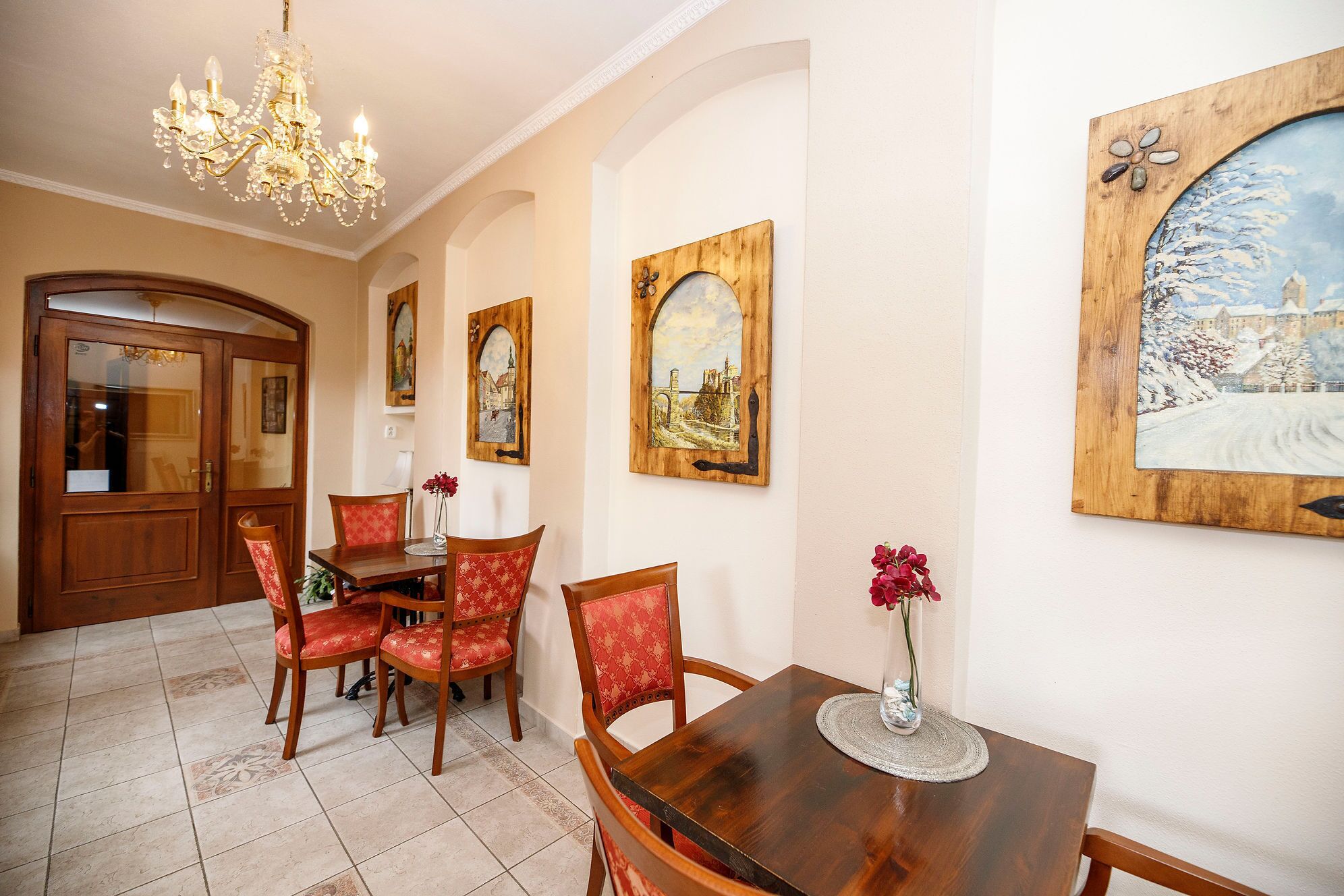 A dining area with a wooden table and chairs, a chandelier, and paintings on the walls.