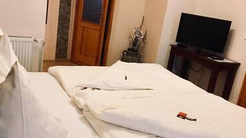 A hotel room with a bed, a television on a stand, a stone wall, and a wooden door.
