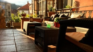 A sunlit outdoor seating area with wicker furniture, potted plants, and a stone lion statue. - Atmosfera (Loket)