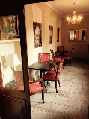 A dining area with a wooden table and red upholstered chairs, a chandelier, and framed artwork on the walls. - Atmosfera (Loket)