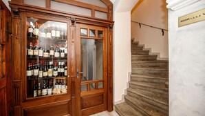 A wooden wine cabinet with multiple shelves of wine bottles, a staircase with a sign indicating room numbers, and a marble floor. - Atmosfera (Loket)