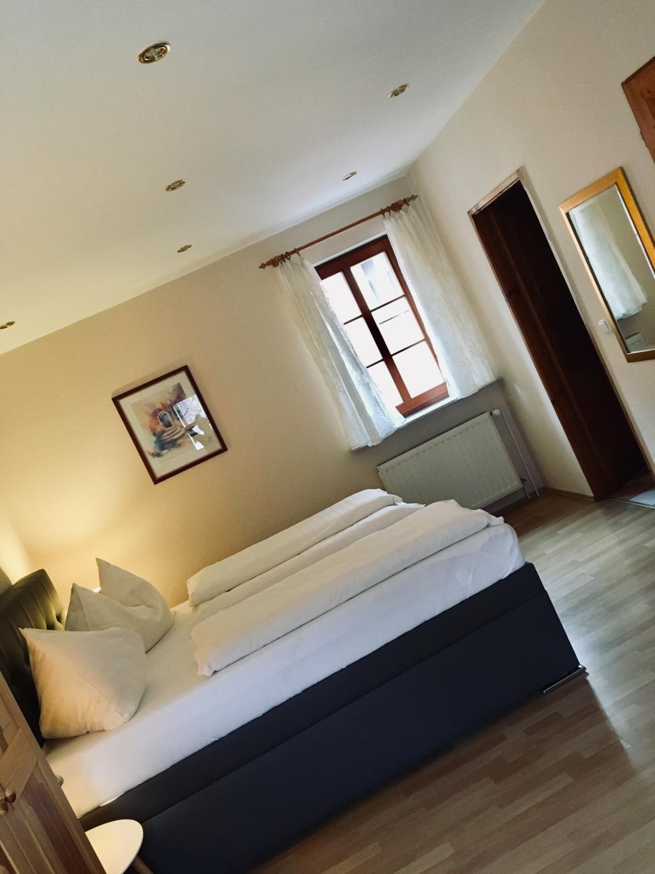 A bedroom with a bed, a window with curtains, a radiator, and a door.