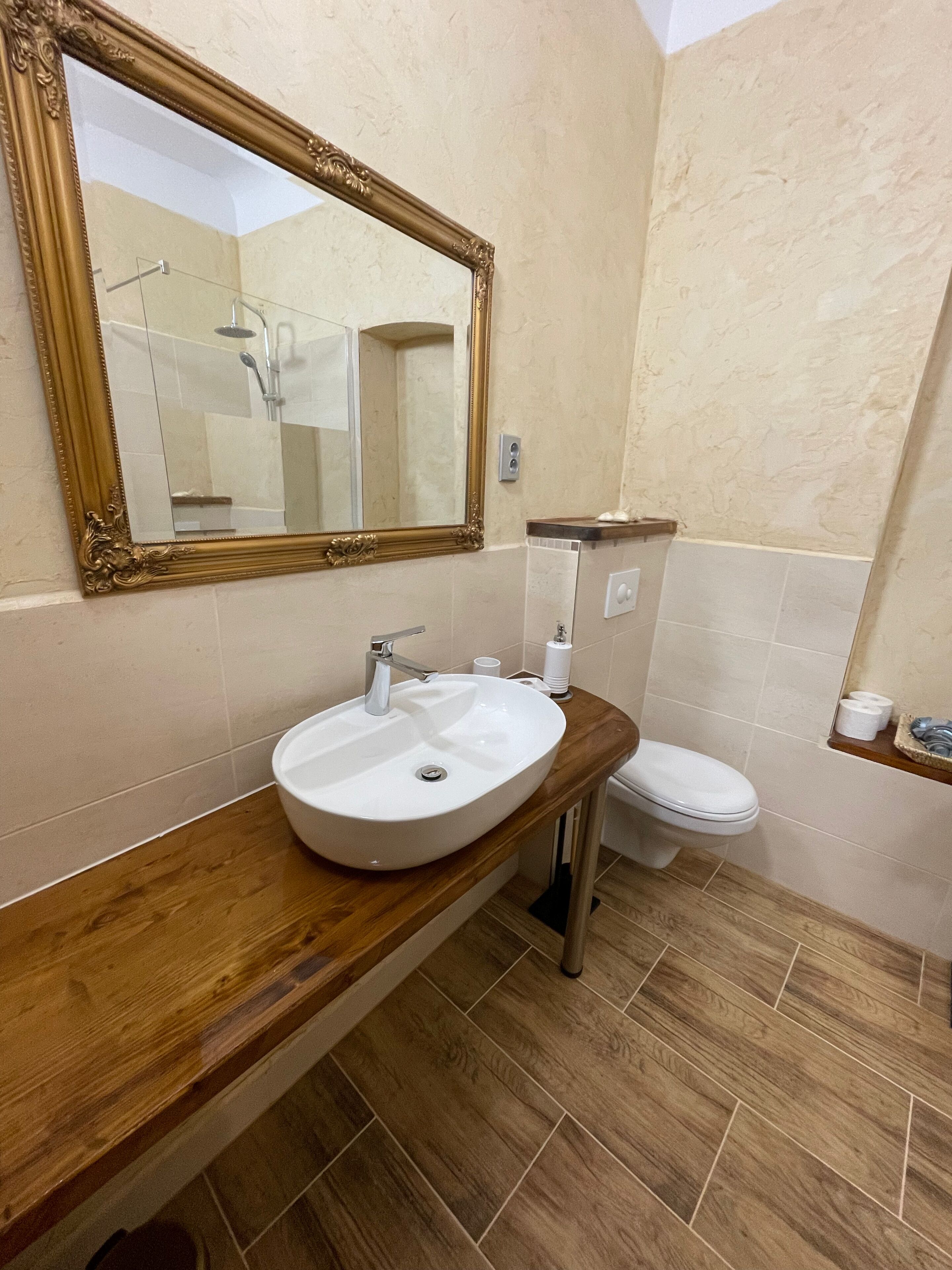 A bathroom with a wooden vanity, a white sink, a toilet, and a mirror with an ornate frame.