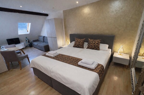A modern hotel room with a large bed, a desk, a sofa, and a TV. - Atmosfera (Loket)