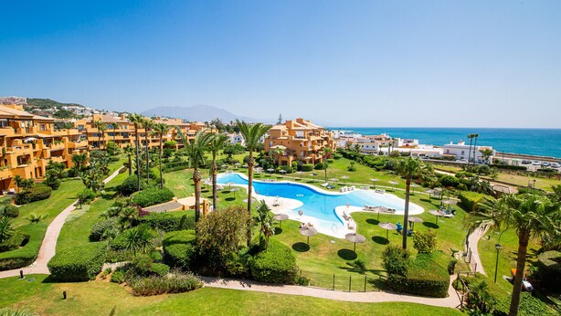 A resort with a swimming pool, lush greenery, and a view of the sea.