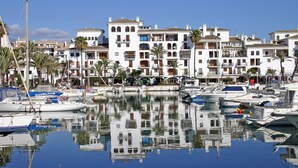 A marina with boats docked, surrounded by white buildings with balconies and palm trees.