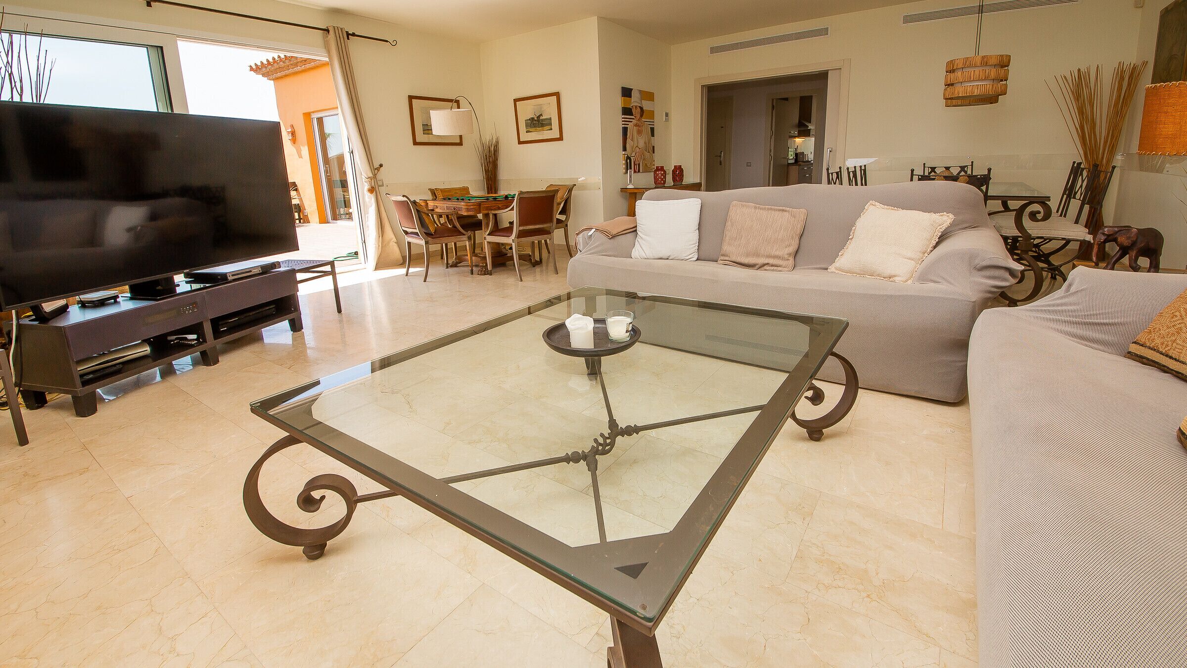 Un salon comprenant une table basse avec un plateau en verre, un canapé, un téléviseur et un coin repas avec des chaises et une table.